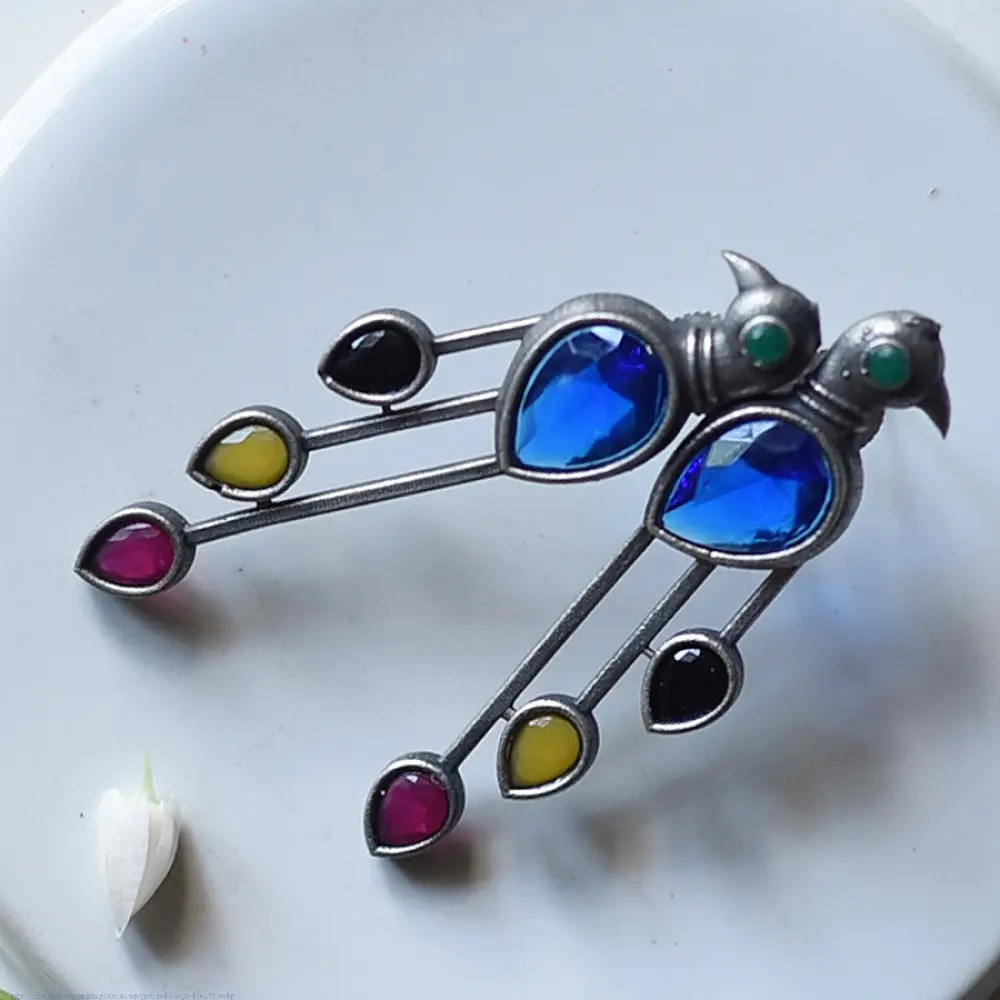 handcrafted german silver bird stud earrings featuring a cobalt blue stone body, jewel-toned glass inlays, and dangling ruby red teardrop tail accent