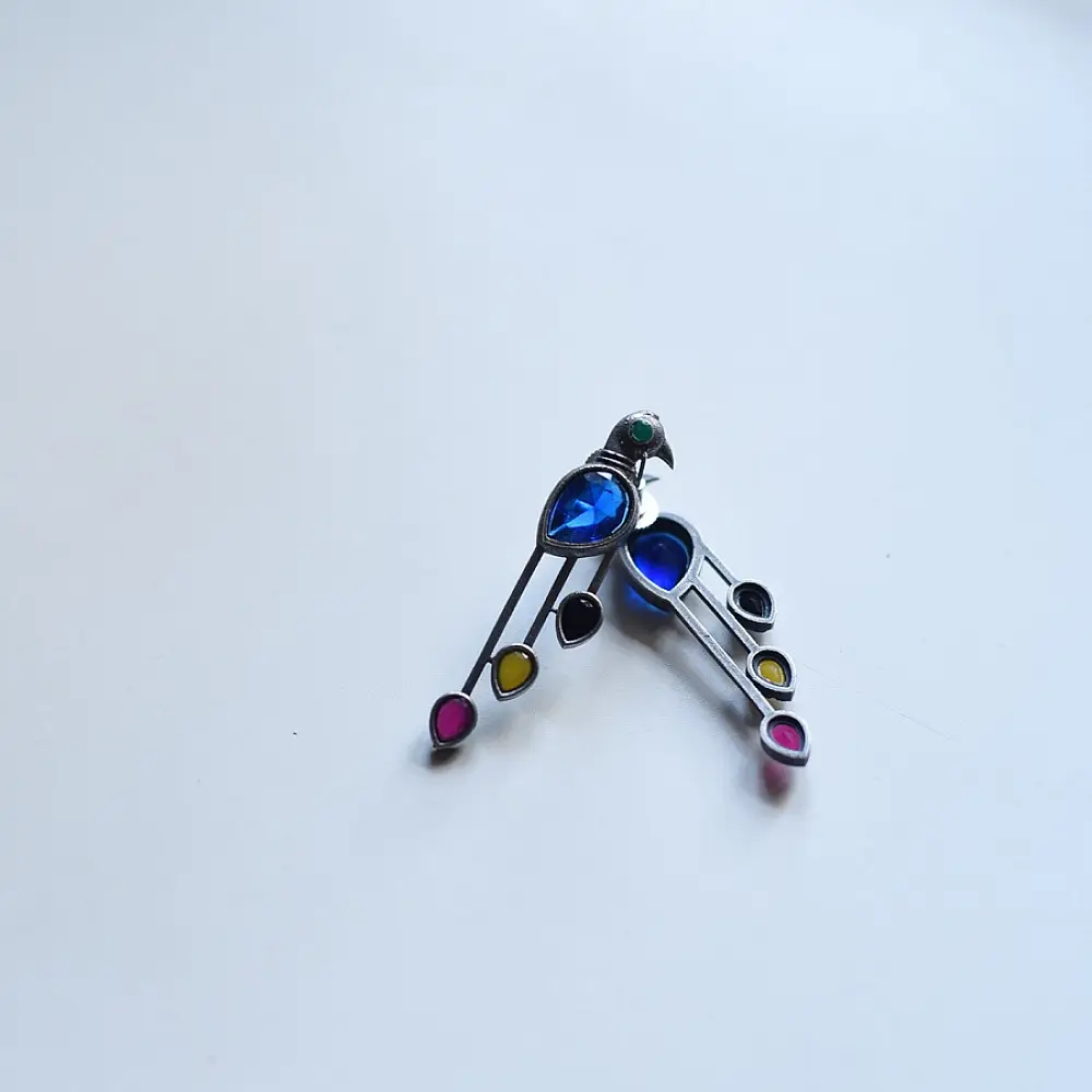 handcrafted german silver bird stud earrings featuring a cobalt blue stone body, jewel-toned glass inlays, and dangling ruby red teardrop tail accent