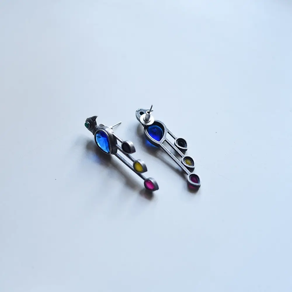 handcrafted german silver bird stud earrings featuring a cobalt blue stone body, jewel-toned glass inlays, and dangling ruby red teardrop tail accent