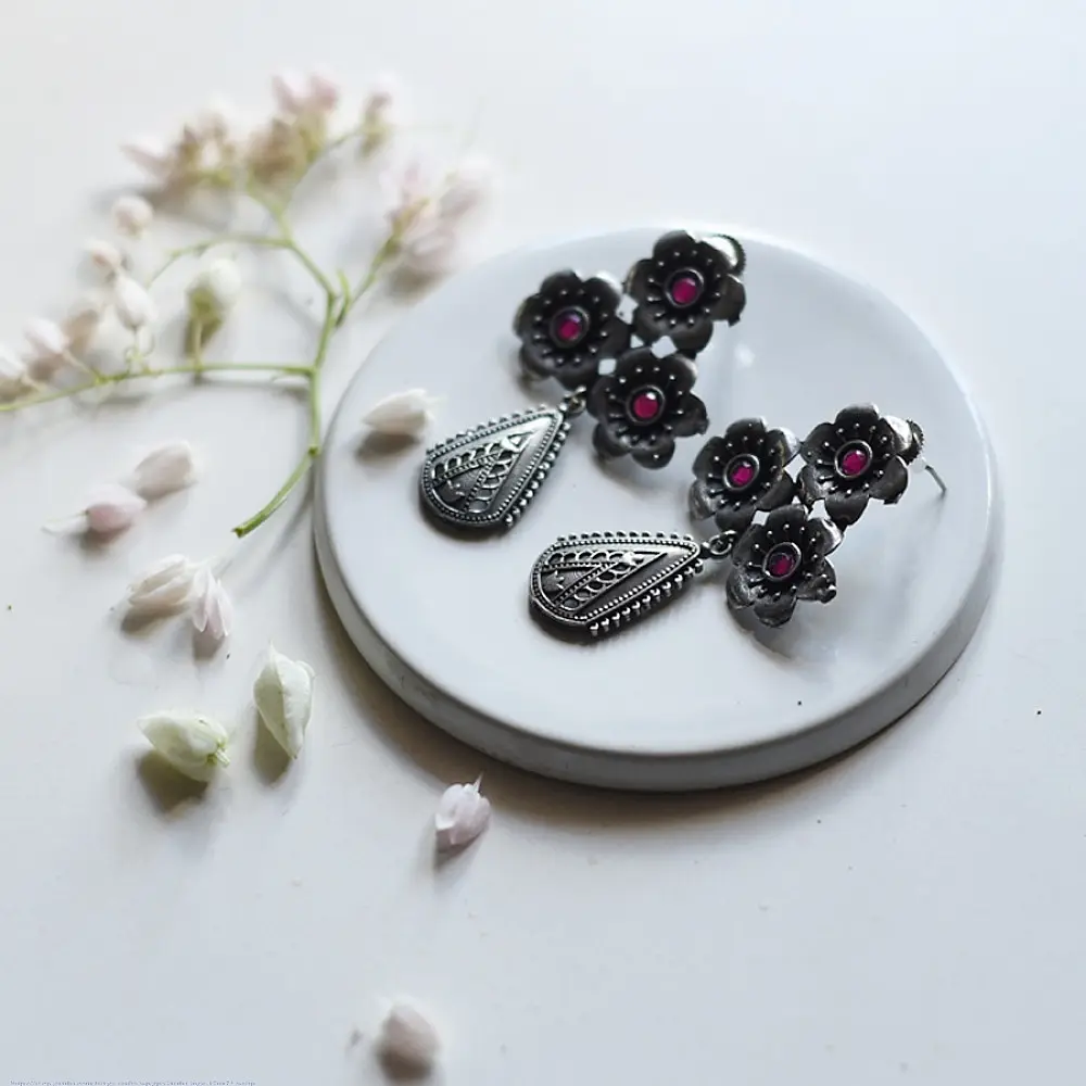 handcrafted german silver drop earrings featuring a floral cluster stud with ruby red stone inlays and a textured, oxidised teardrop pendant