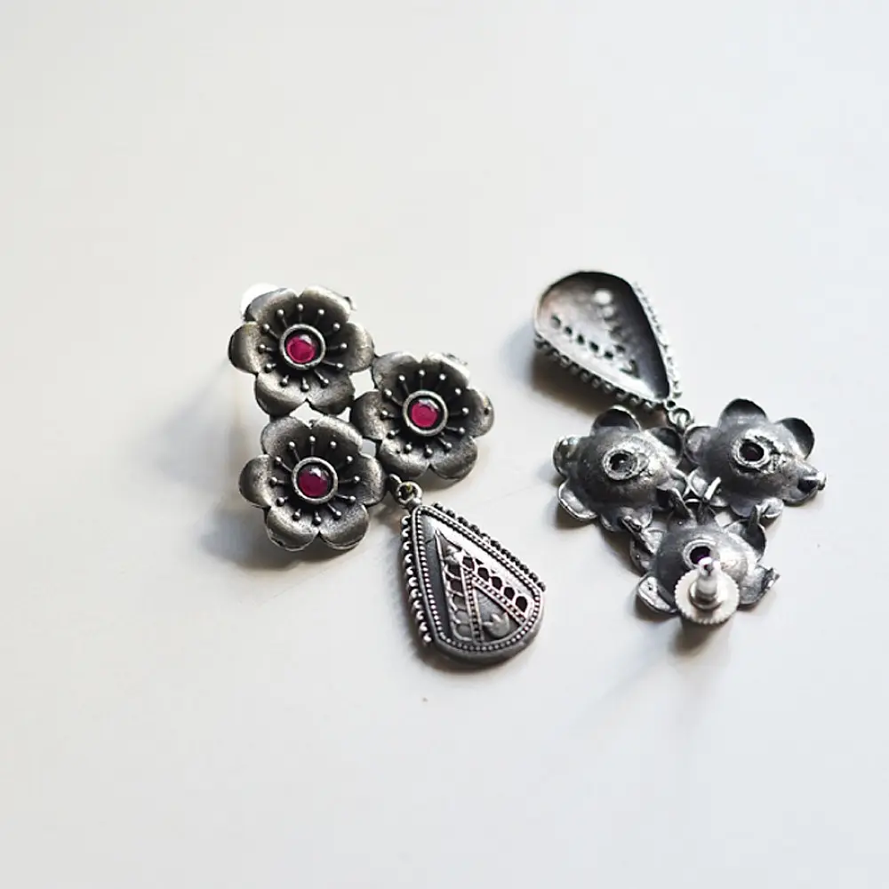 handcrafted german silver drop earrings featuring a floral cluster stud with ruby red stone inlays and a textured, oxidised teardrop pendant