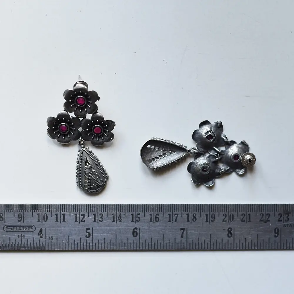 handcrafted german silver drop earrings featuring a floral cluster stud with ruby red stone inlays and a textured, oxidised teardrop pendant