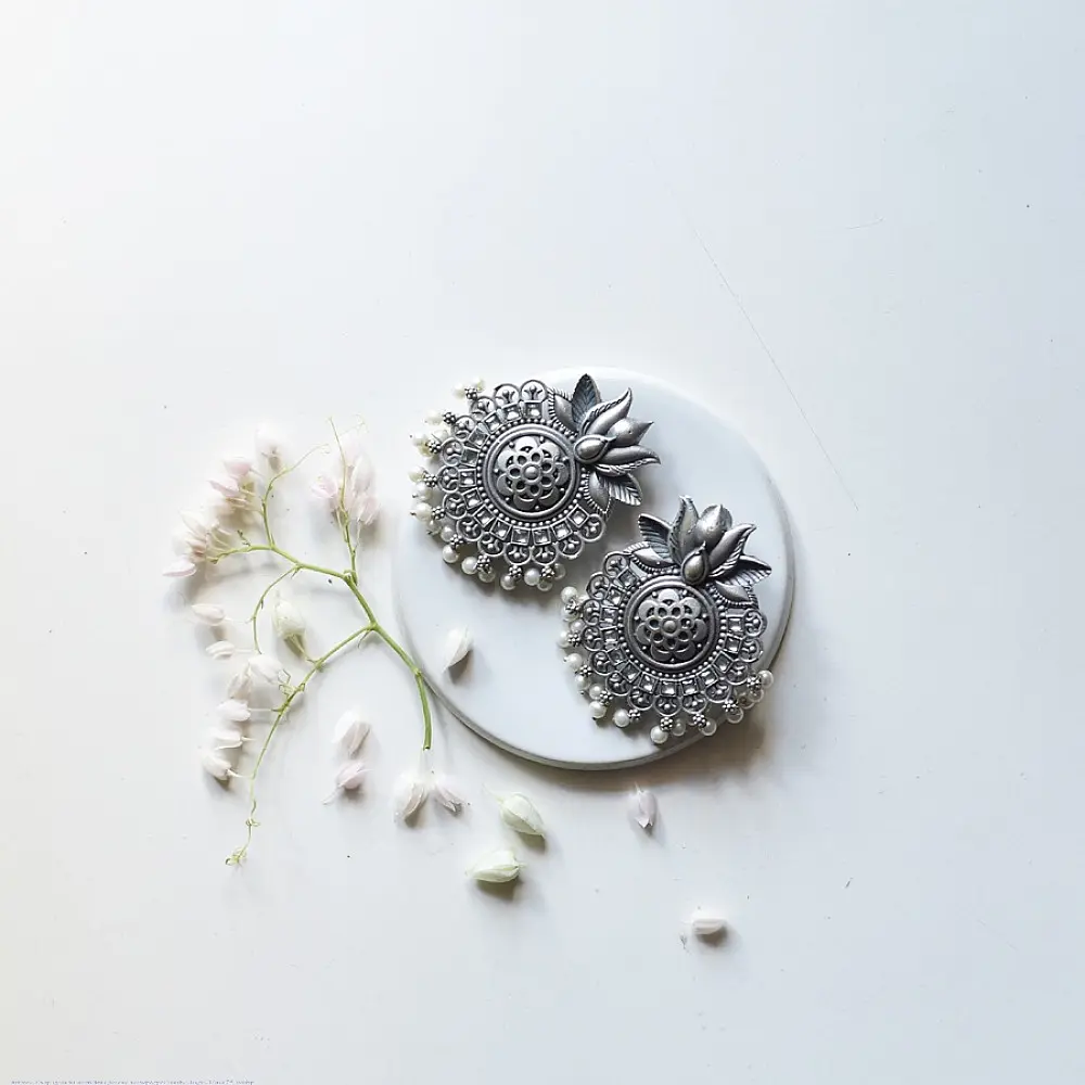 handcrafted german silver lotus motif stud earrings featuring a textured circular centerpiece, radiating petal border, crown leaf crest, and dangling pearl ghungroos