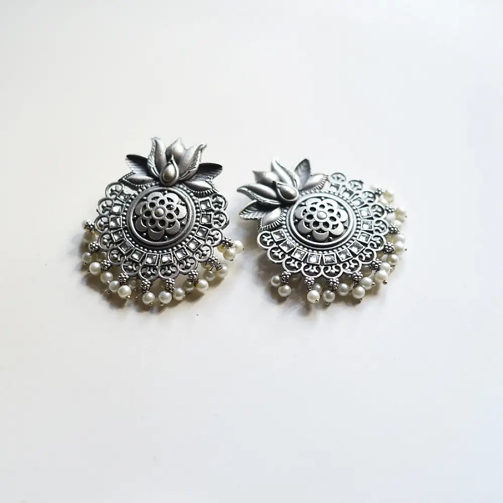 handcrafted german silver lotus motif stud earrings featuring a textured circular centerpiece, radiating petal border, crown leaf crest, and dangling pearl ghungroos