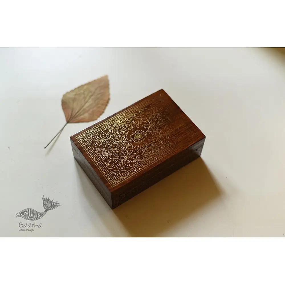 handcrafted rectangular wooden box featuring complex brass wire Tarkashi inlay work forming a central paisley floral layout and bordering coin circles next to a dry leaf