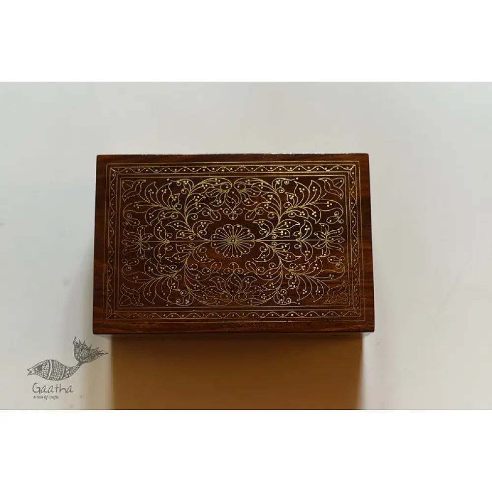 handcrafted rectangular wooden box featuring complex brass wire Tarkashi inlay work forming a central paisley floral layout and bordering coin circles next to a dry leaf