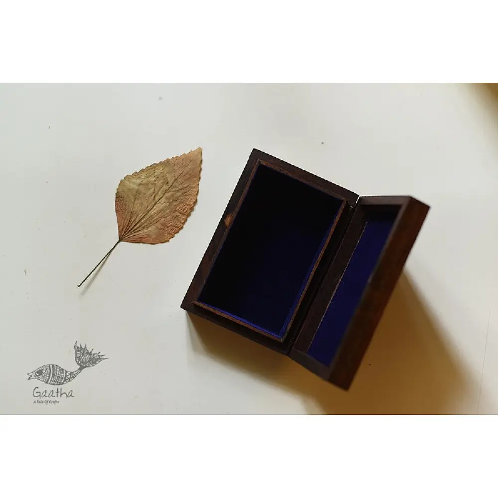 handcrafted rectangular wooden box featuring complex brass wire Tarkashi inlay work forming a central paisley floral layout and bordering coin circles next to a dry leaf