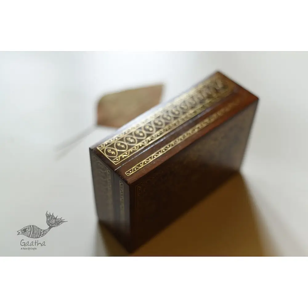 handcrafted rectangular wooden box featuring complex brass wire Tarkashi inlay work forming a central paisley floral layout and bordering coin circles next to a dry leaf