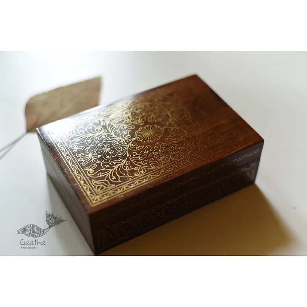 handcrafted rectangular wooden box featuring complex brass wire Tarkashi inlay work forming a central paisley floral layout and bordering coin circles next to a dry leaf