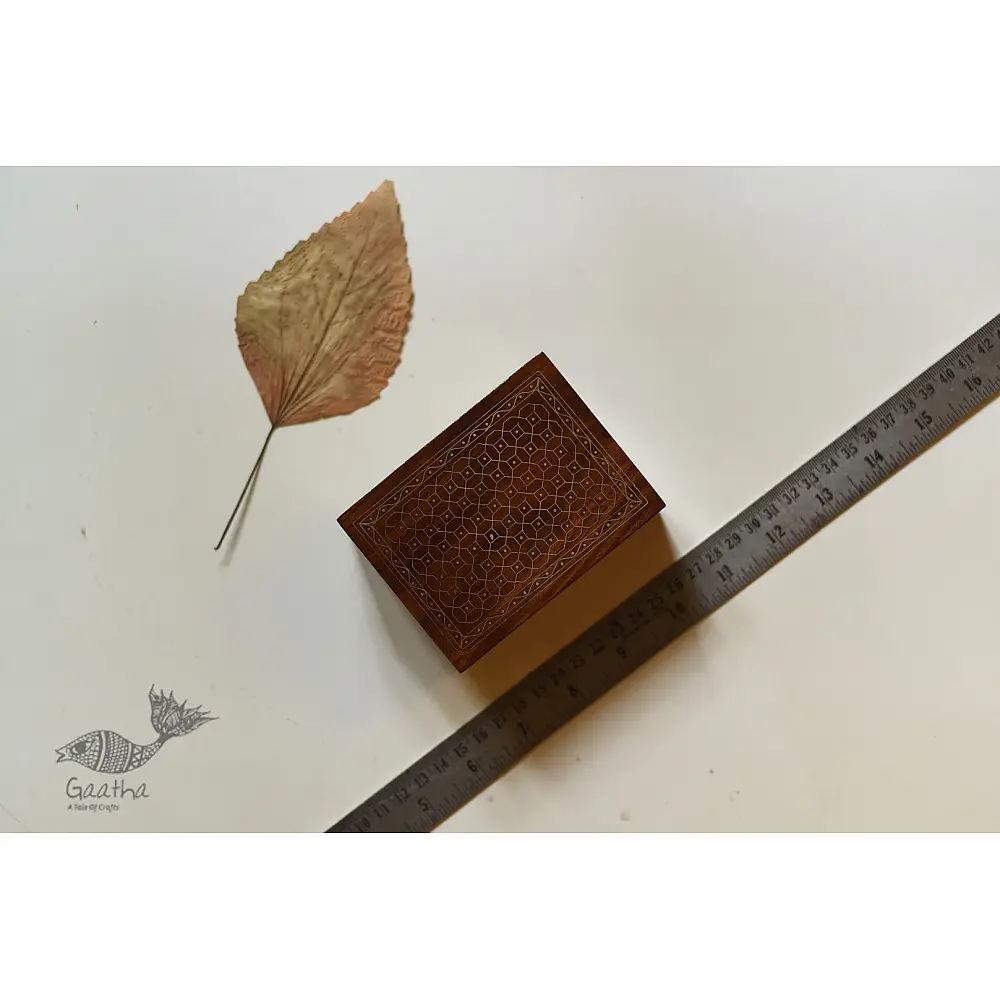 handcrafted rectangular wooden box with complex geometric brass wire Tarkashi inlay work forming an interconnected hexagonal lattice design across the polished lid next to a dry leaf