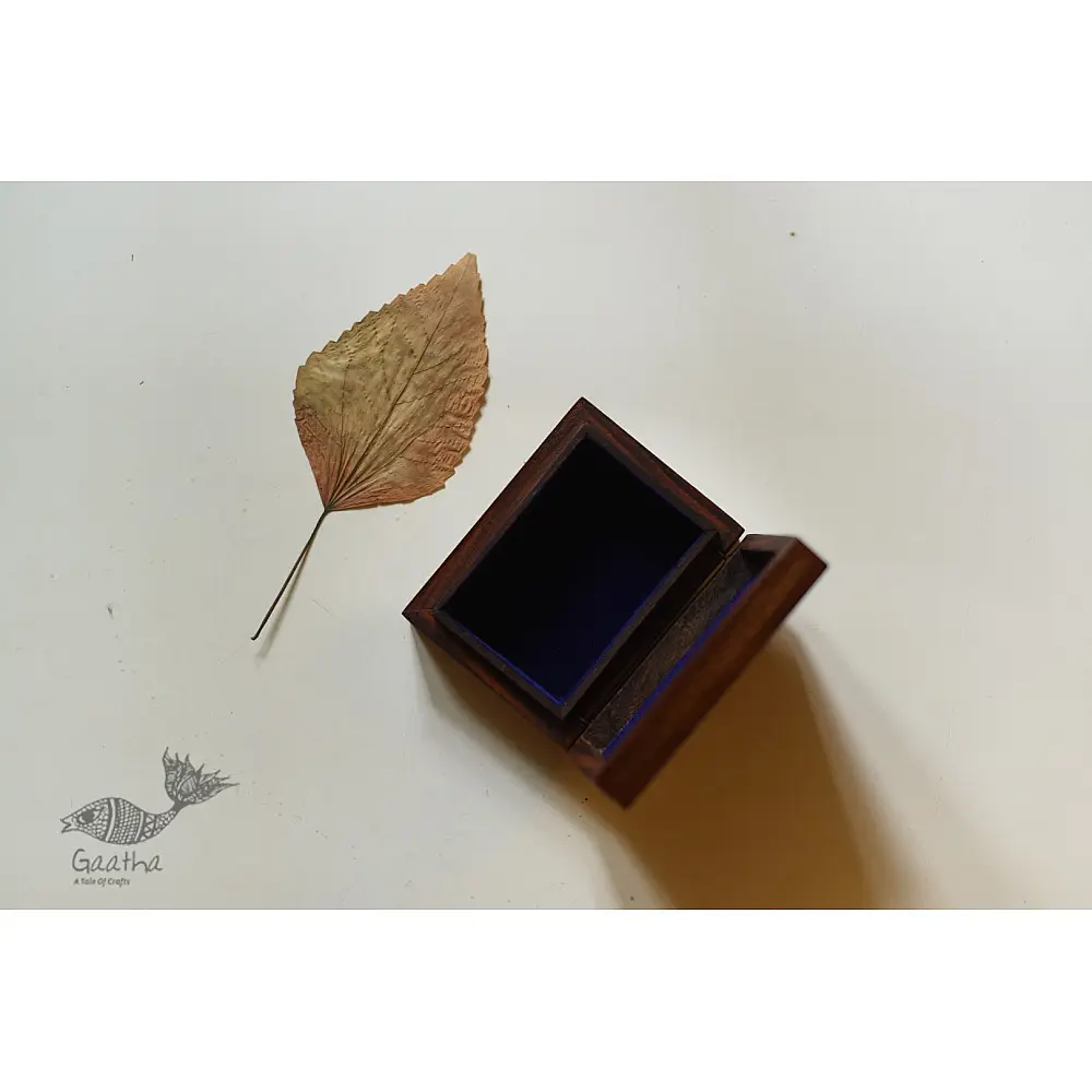 handcrafted rectangular wooden box with complex geometric brass wire Tarkashi inlay work forming an interconnected hexagonal lattice design across the polished lid next to a dry leaf