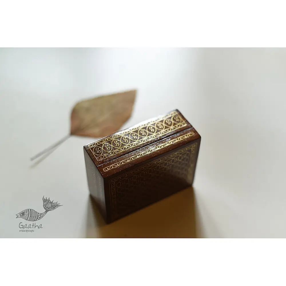 handcrafted rectangular wooden box with complex geometric brass wire Tarkashi inlay work forming an interconnected hexagonal lattice design across the polished lid next to a dry leaf
