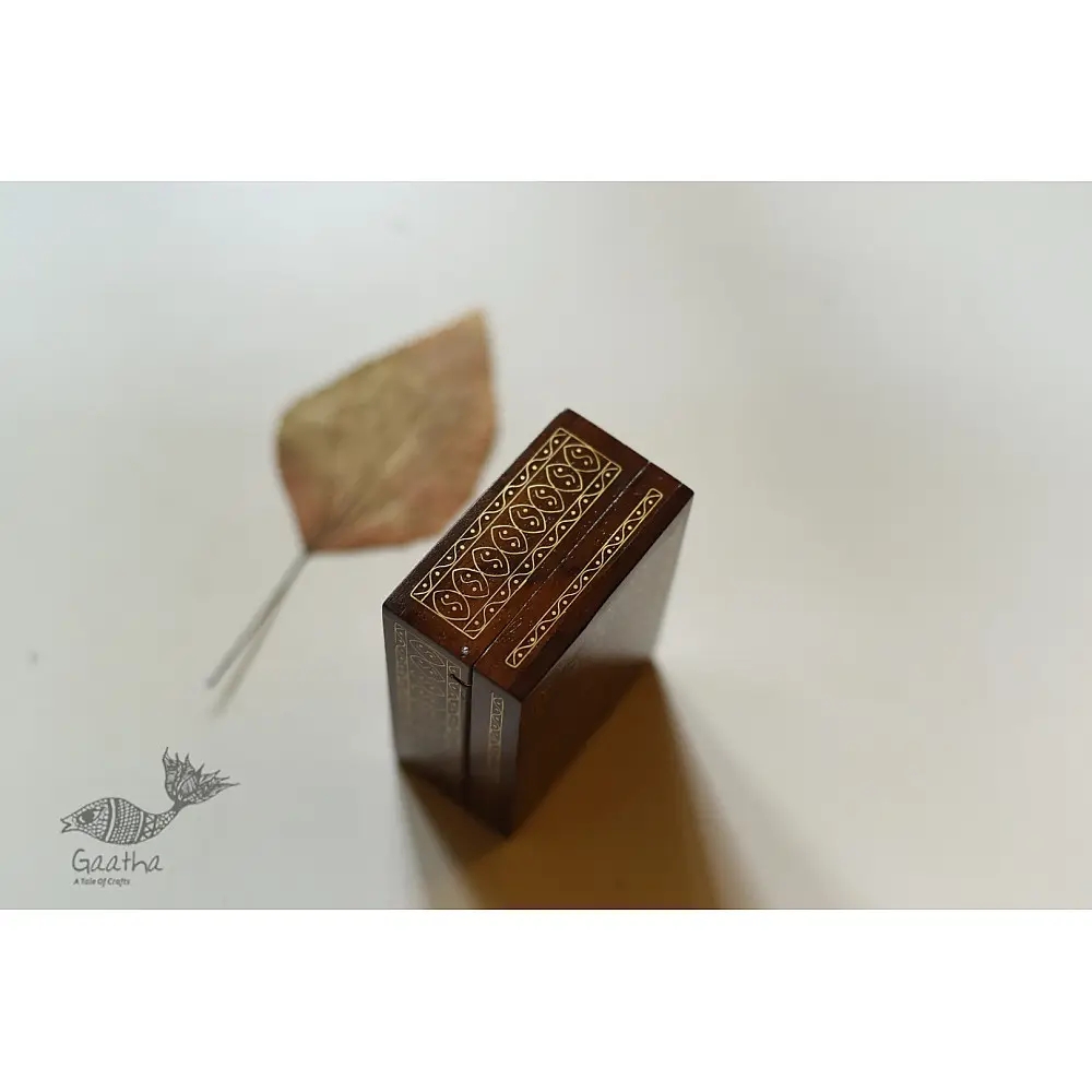 handcrafted rectangular wooden box with complex geometric brass wire Tarkashi inlay work forming an interconnected hexagonal lattice design across the polished lid next to a dry leaf