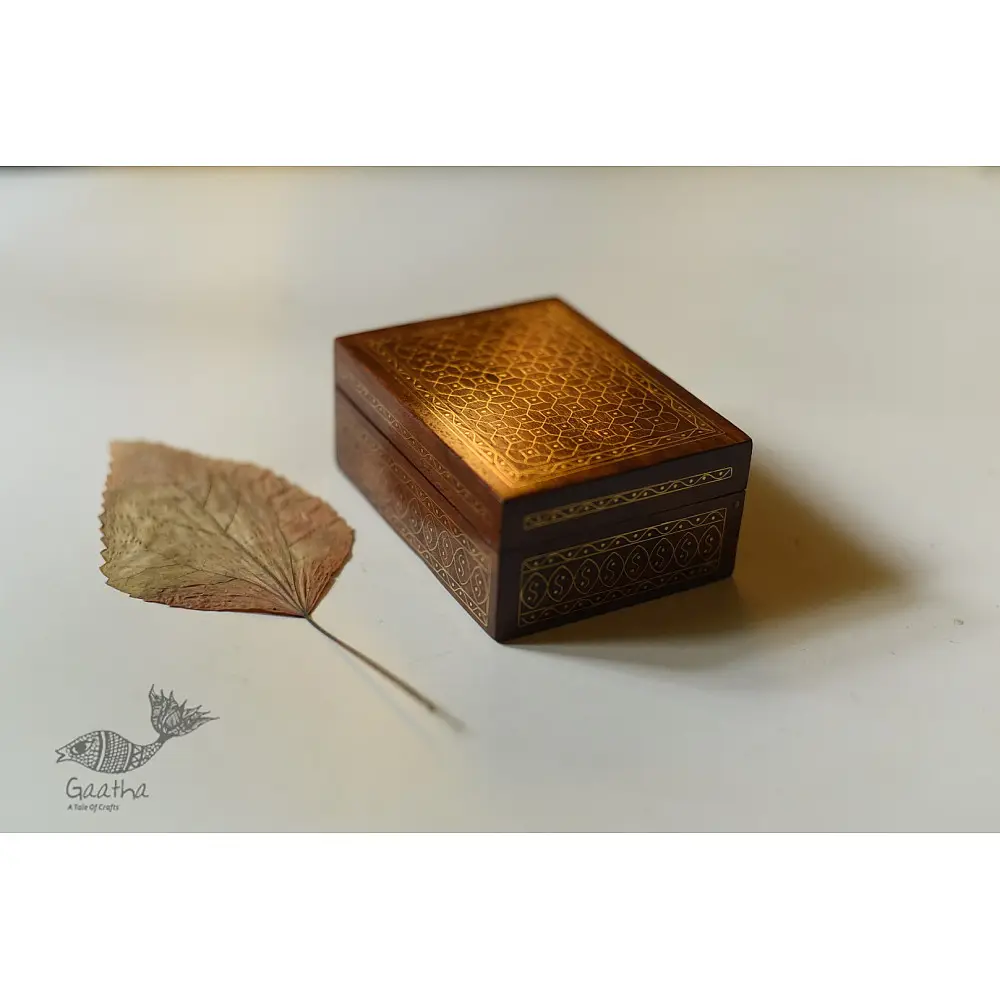 handcrafted rectangular wooden box with complex geometric brass wire Tarkashi inlay work forming an interconnected hexagonal lattice design across the polished lid next to a dry leaf