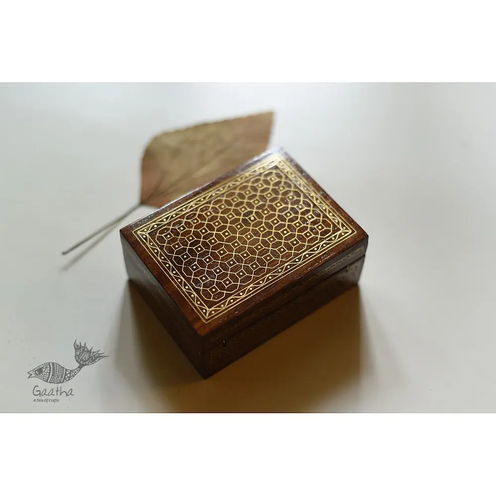 handcrafted rectangular wooden box with complex geometric brass wire Tarkashi inlay work forming an interconnected hexagonal lattice design across the polished lid next to a dry leaf