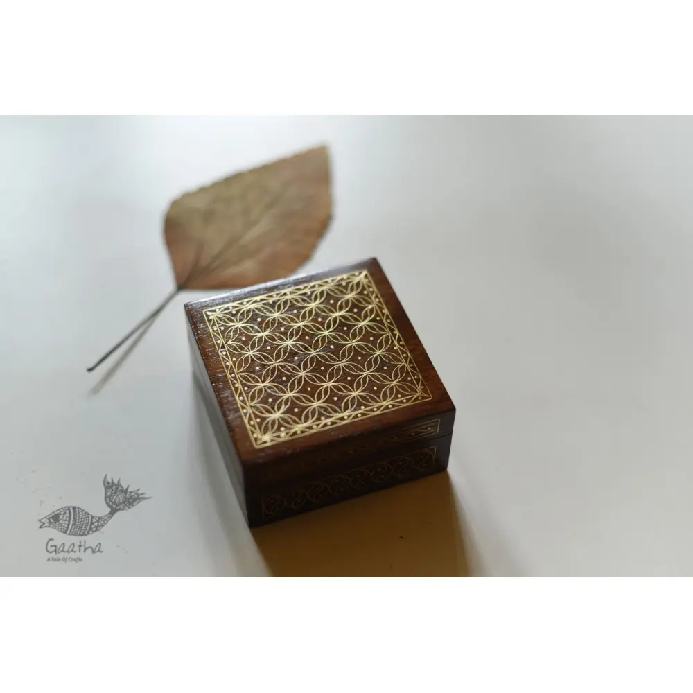 handcrafted square wood gift box with intricate geometric brass wire Tarkashi inlay work forming a repeating overlapping circle pattern across the polished lid next to a dry leaf