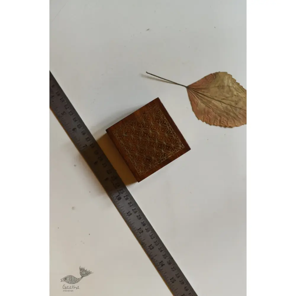 handcrafted square wood gift box with intricate geometric brass wire Tarkashi inlay work forming a repeating overlapping circle pattern across the polished lid next to a dry leaf