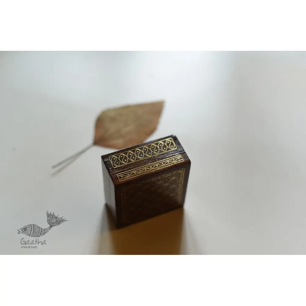 handcrafted square wood gift box with intricate geometric brass wire Tarkashi inlay work forming a repeating overlapping circle pattern across the polished lid next to a dry leaf
