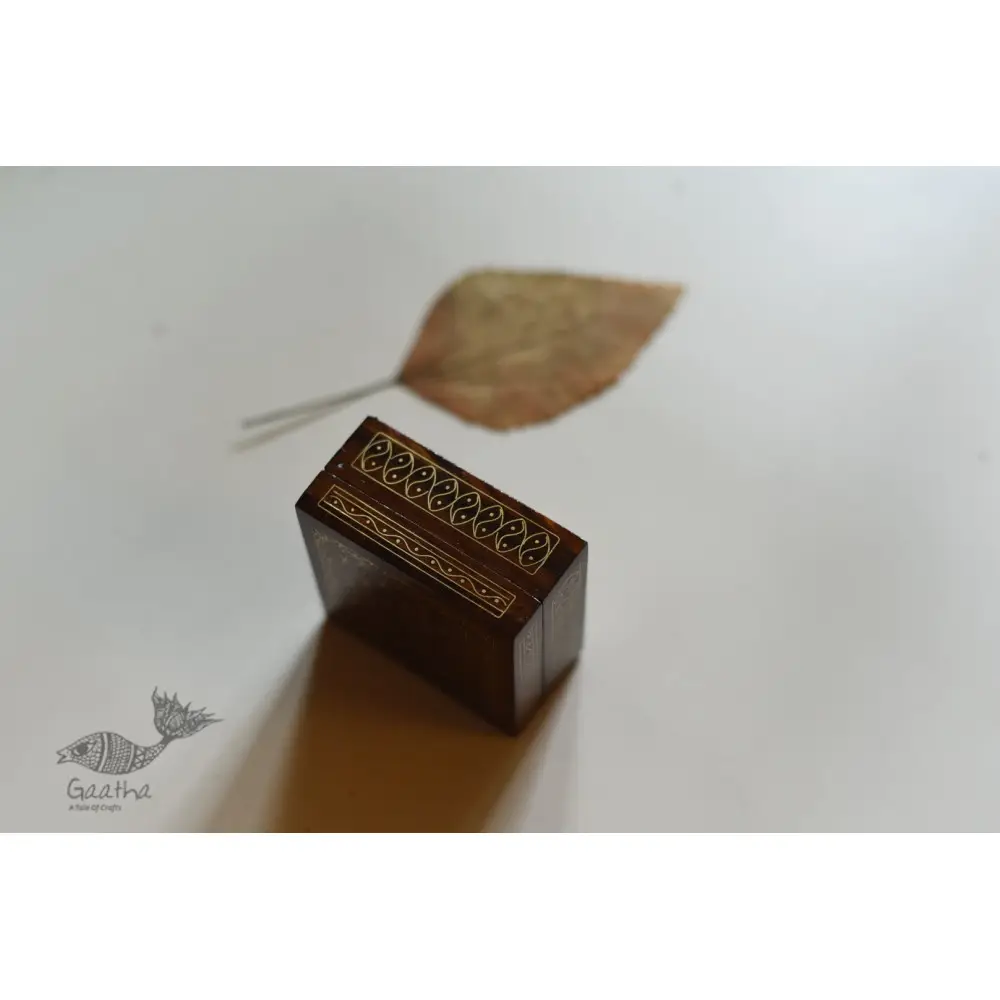 handcrafted square wood gift box with intricate geometric brass wire Tarkashi inlay work forming a repeating overlapping circle pattern across the polished lid next to a dry leaf