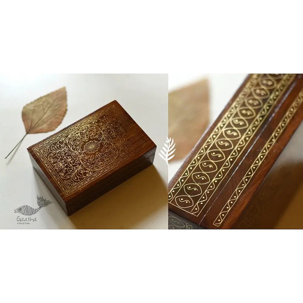 handcrafted rectangular wooden box featuring complex brass wire Tarkashi inlay work forming a central paisley floral layout and bordering coin circles next to a dry leaf