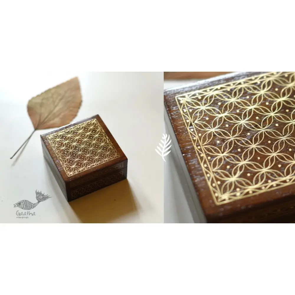 handcrafted square wood gift box with intricate geometric brass wire Tarkashi inlay work forming a repeating overlapping circle pattern across the polished lid next to a dry leaf