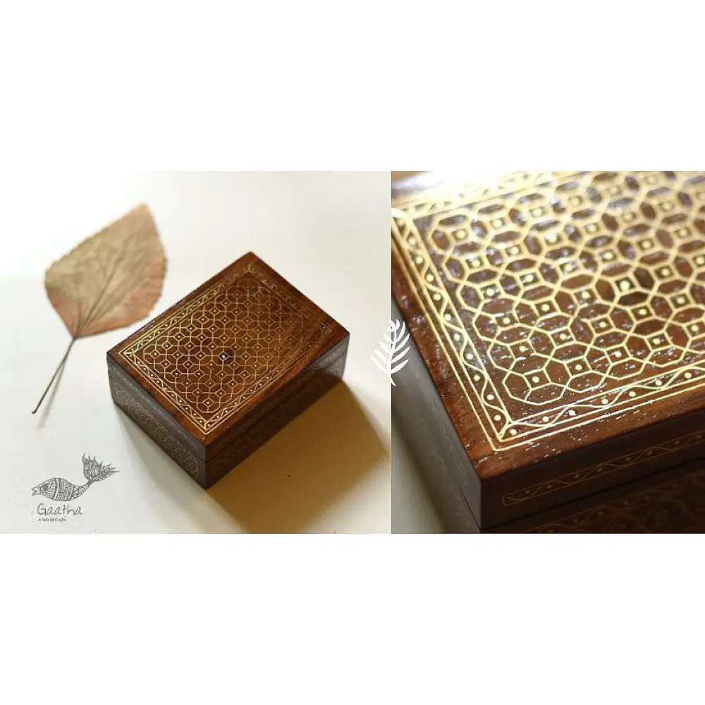 handcrafted rectangular wooden box with complex geometric brass wire Tarkashi inlay work forming an interconnected hexagonal lattice design across the polished lid next to a dry leaf