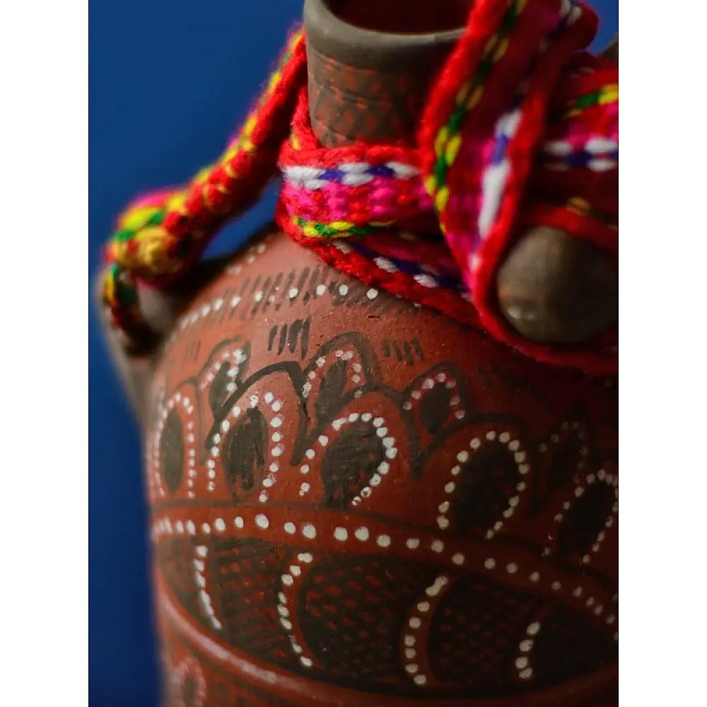 terracotta water bottle with white hand-painted geometric motifs and multicolour cord wrapped neck