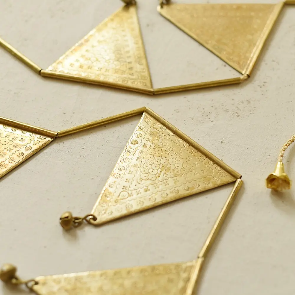 handmade brass triangle design toran door hanging featuring pennant shaped brass flags linked on a brass chain with central floral pendant drop   