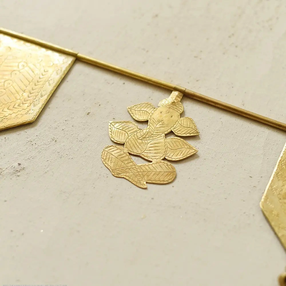 handmade brass toran door hanging featuring geometric brass flags linked on a brass chain with a central floral motif pendant