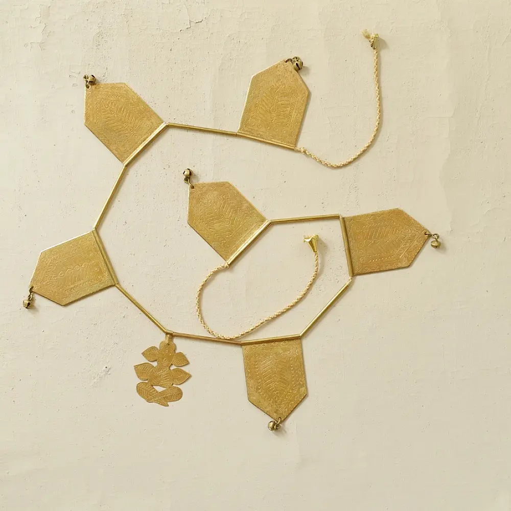 handmade brass toran door hanging featuring geometric brass flags linked on a brass chain with a central floral motif pendant