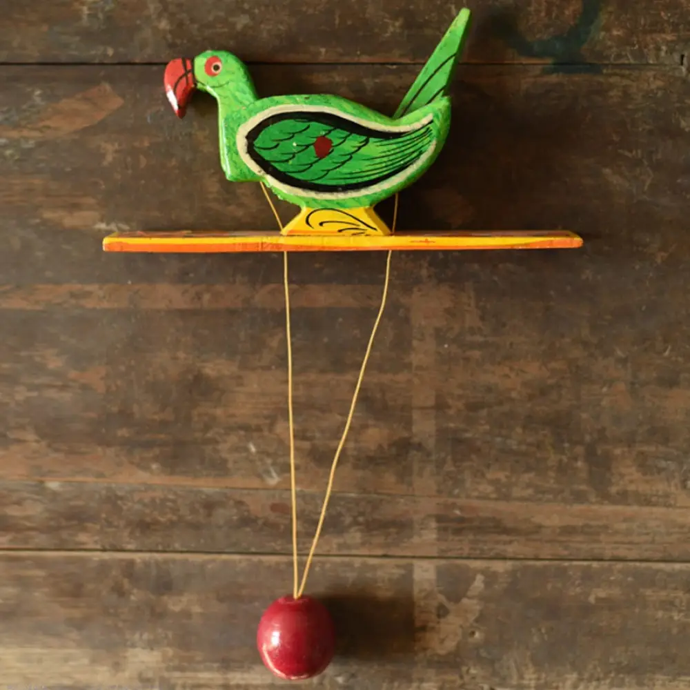handcrafted wooden moving parrot toy painted in traditional green and red with a dangling weight mechanism