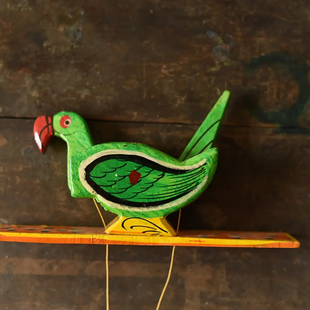 handcrafted wooden moving parrot toy painted in traditional green and red with a dangling weight mechanism