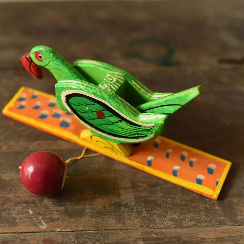 handcrafted wooden moving parrot toy painted in traditional green and red with a dangling weight mechanism