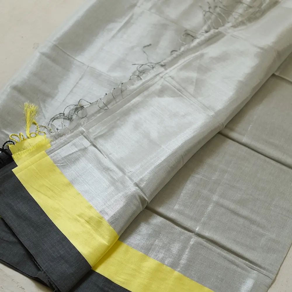 handloom pure cotton saree in soft grey and white featuring a bright lemon yellow color blocked panel with a black striped zari border and handcrafted tassels