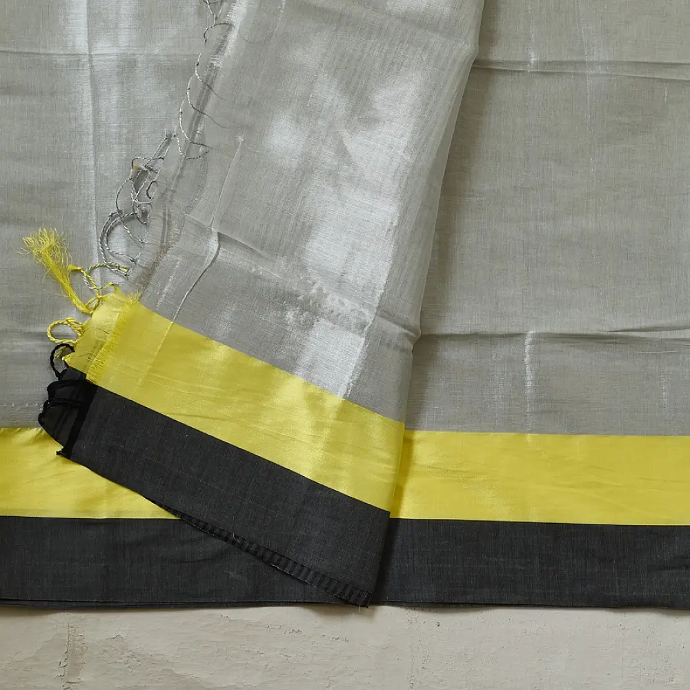 handloom pure cotton saree in soft grey and white featuring a bright lemon yellow color blocked panel with a black striped zari border and handcrafted tassels