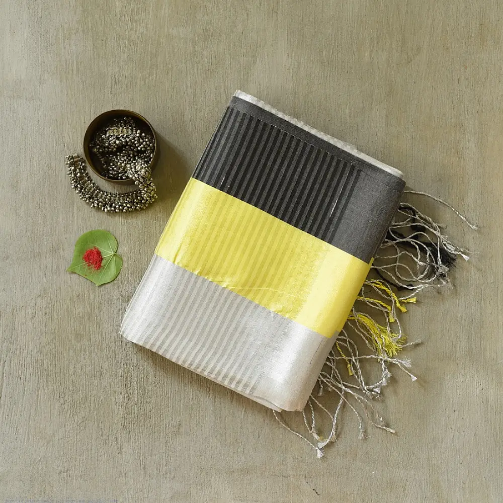handloom pure cotton saree in soft grey and white featuring a bright lemon yellow color blocked panel with a black striped zari border and handcrafted tassels