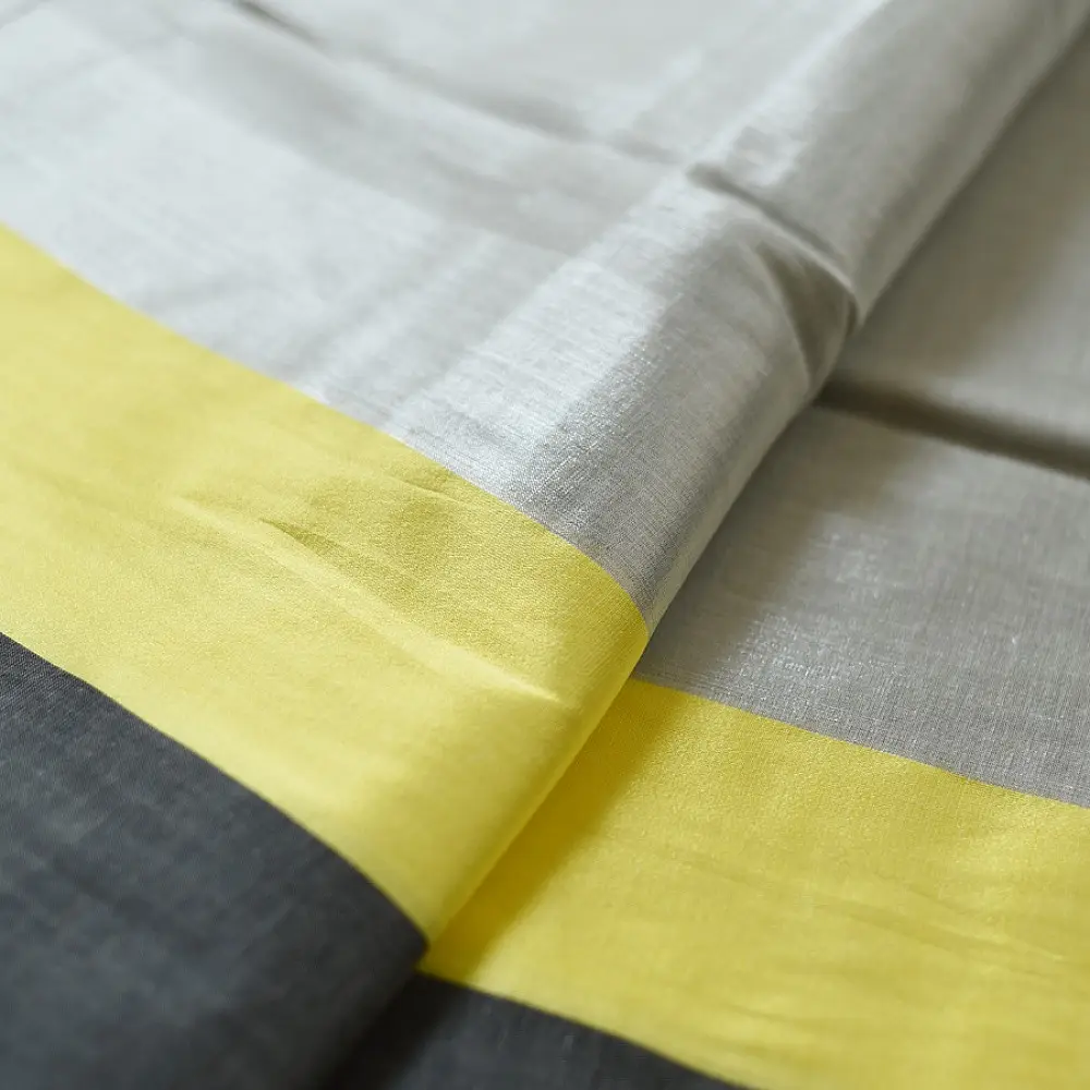 handloom pure cotton saree in soft grey and white featuring a bright lemon yellow color blocked panel with a black striped zari border and handcrafted tassels