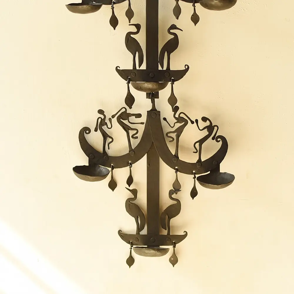 handcrafted black wrought iron wall hanging lamp featuring a tiered vertical chain design with stylized tribal figures and oil diya cups