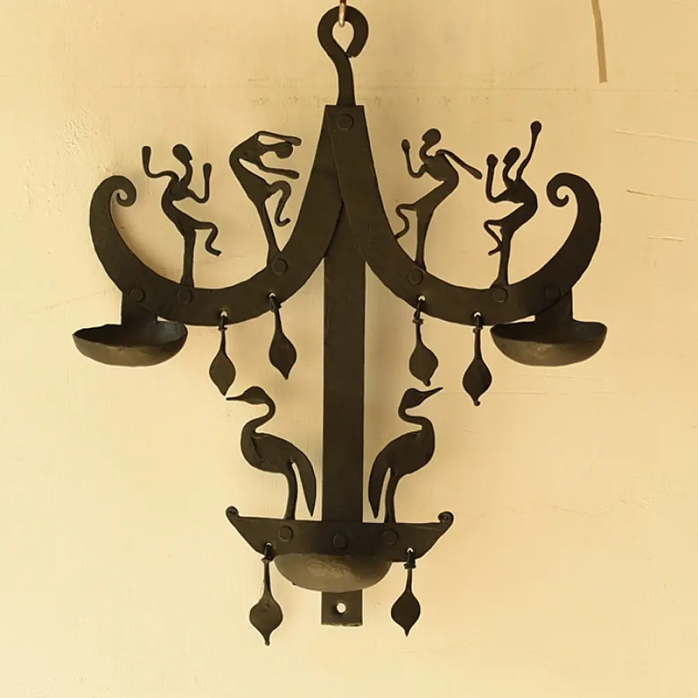 handcrafted black wrought iron wall hanging lamp featuring a tiered vertical chain design with stylized tribal figures and oil diya cups