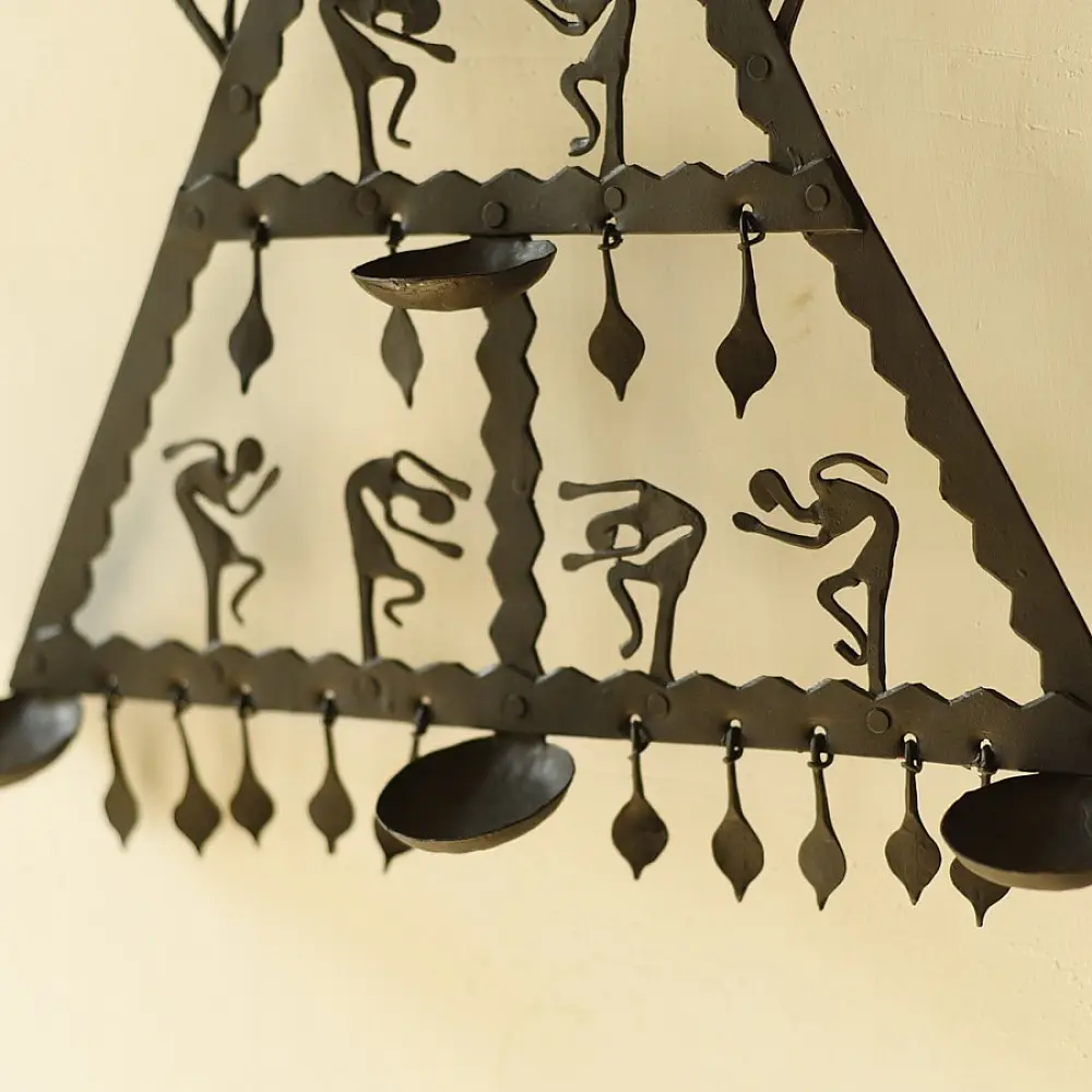 handcrafted black wrought iron triangular hanging lamp featuring multi-tier compartments with dancing tribal figures and hanging oil diya cups