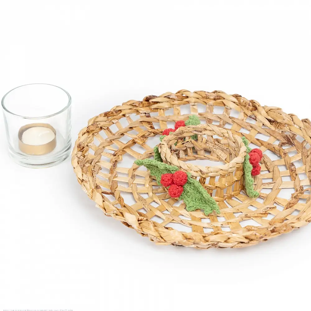 handcrafted banana fiber woven candle wreath centerpiece with a glass tealight holder cup and green and red crochet holly berry accents on a dining table layout