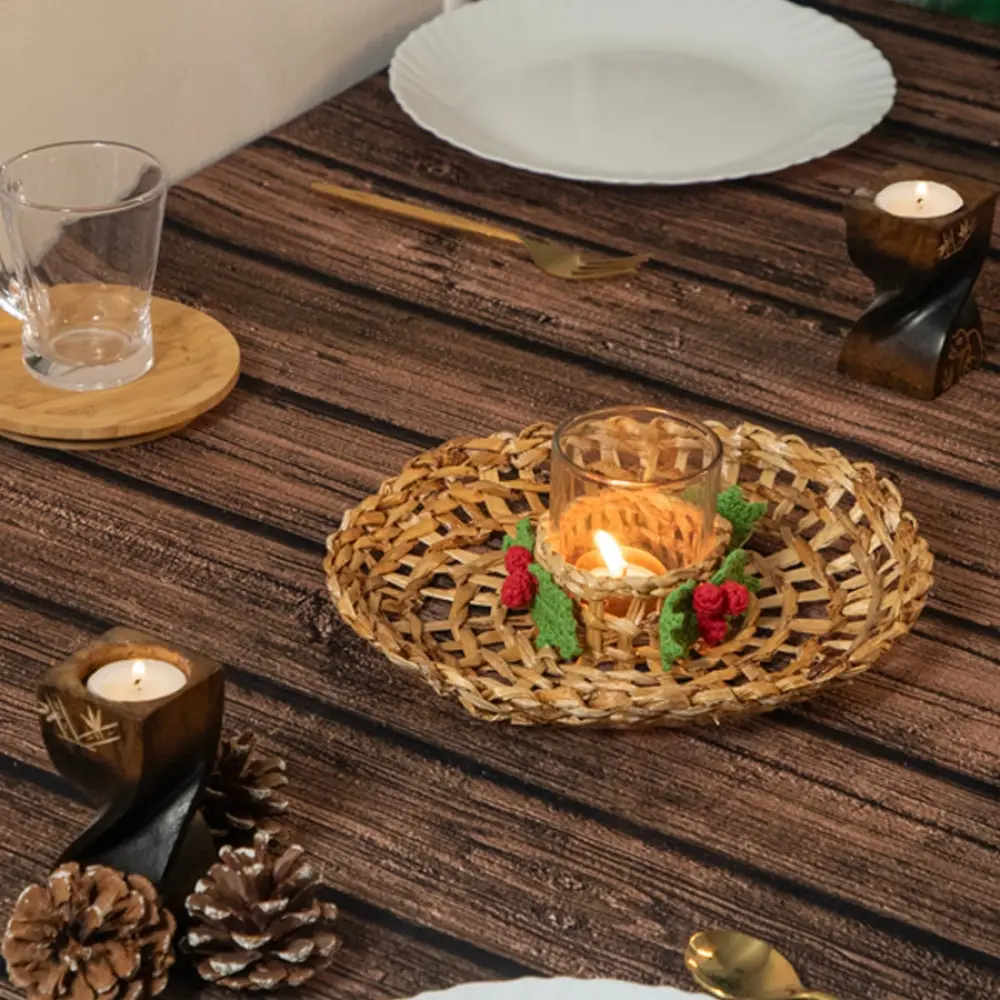 handcrafted banana fiber woven candle wreath centerpiece with a glass tealight holder cup and green and red crochet holly berry accents on a dining table layout