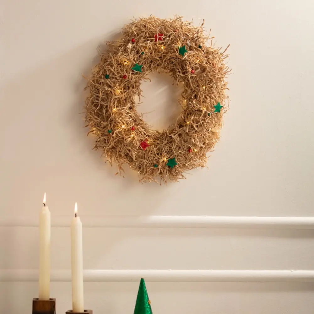 handcrafted banana fiber frill circular christmas wreath accented with miniature red and green star decorations against a neutral background wall