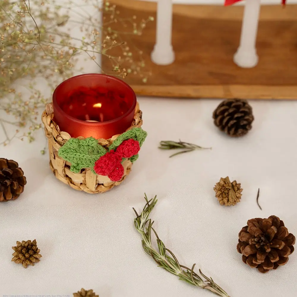 handcrafted banana bark woven tea light holders with green and red crochet holly berry accents holding colored glass candle cups on a festive table display