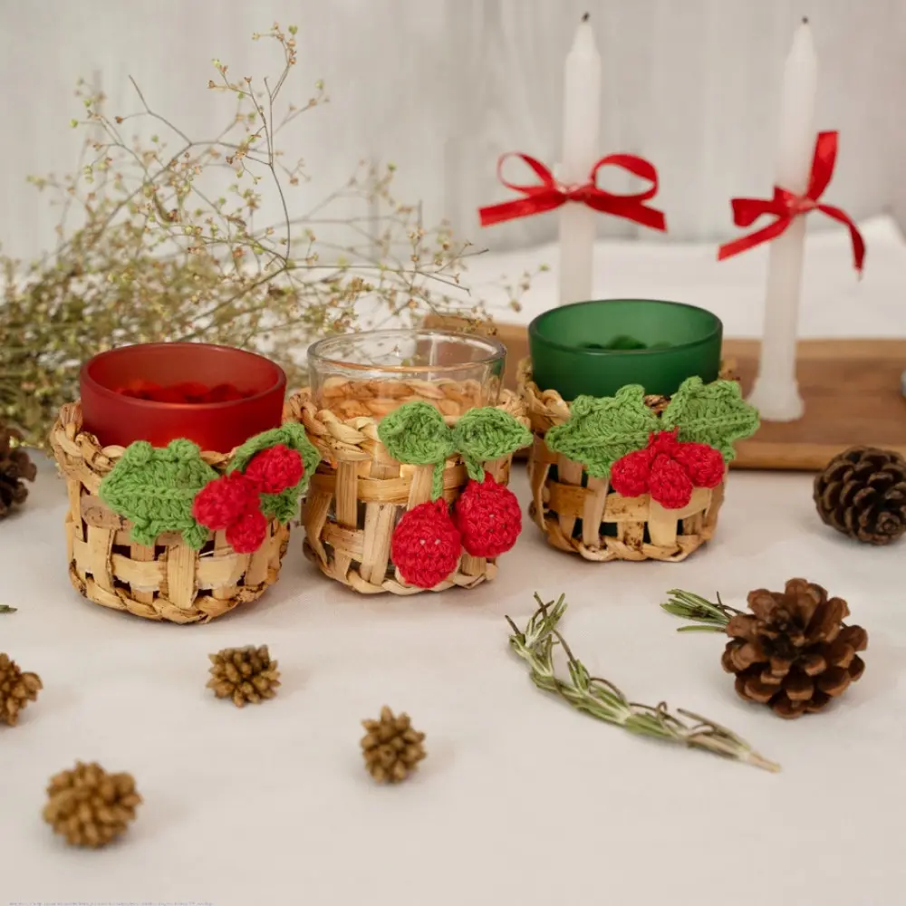 handcrafted banana bark woven tea light holders with green and red crochet holly berry accents holding colored glass candle cups on a festive table display