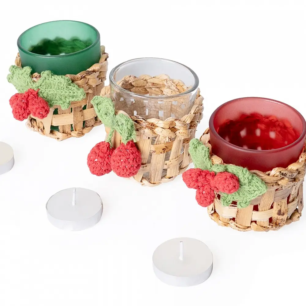 handcrafted banana bark woven tea light holders with green and red crochet holly berry accents holding colored glass candle cups on a festive table display