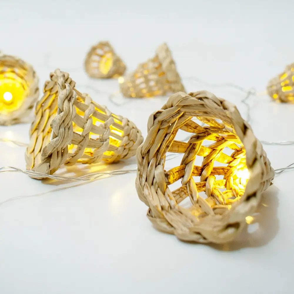 handcrafted banana bark fiber bell fairy lights emitting a warm amber glow against a textured white brick wall pattern