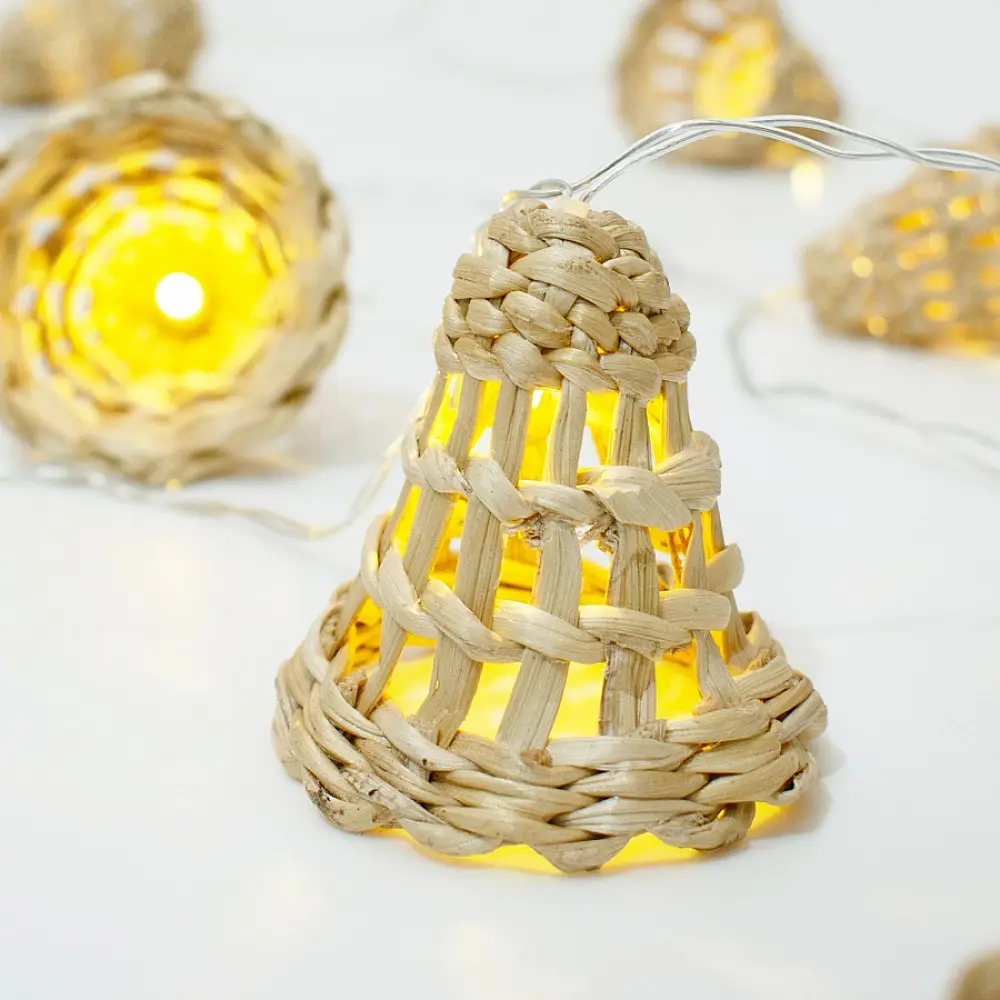 handcrafted banana bark fiber bell fairy lights emitting a warm amber glow against a textured white brick wall pattern