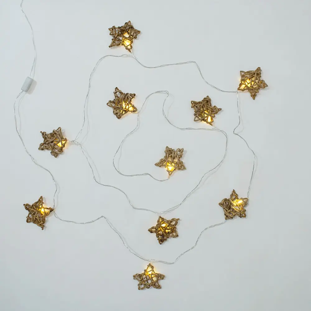 handcrafted banana bark fiber bell fairy lights emitting a warm amber glow against a textured white brick wall pattern