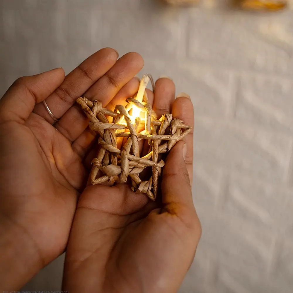 handcrafted banana fiber rope star fairy lights emitting a warm amber glow against a textured white brick wall pattern